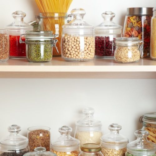 Glass jars with different types of groats and pasta on wooden shelves
